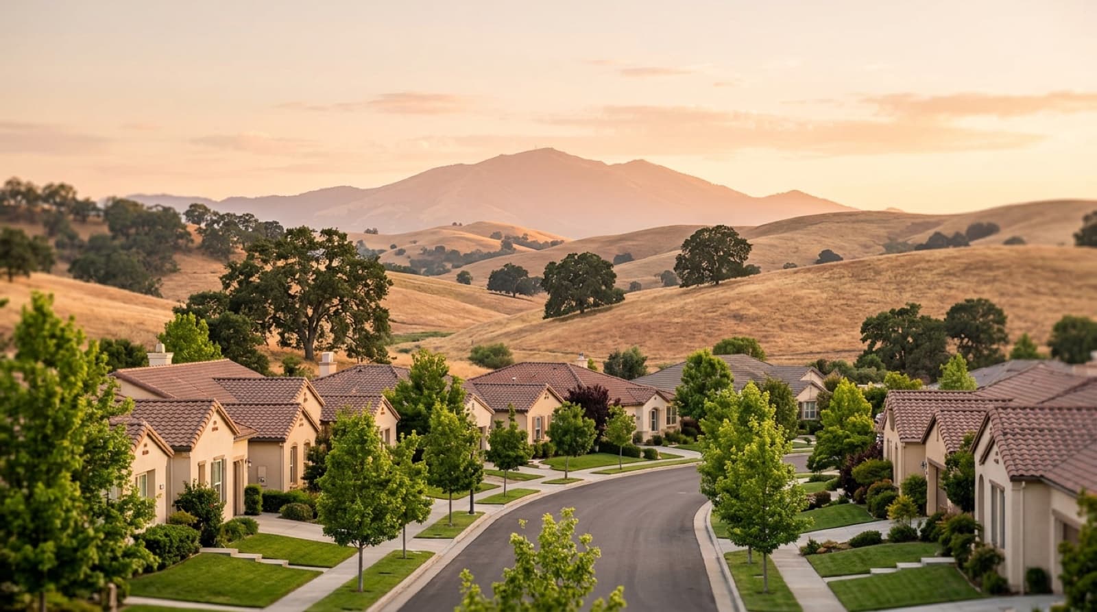 A curving Brentwood street of single-story tile-roof homes at golden hour, with dry golden hills, oak trees, and Mount Diablo in the distance.
